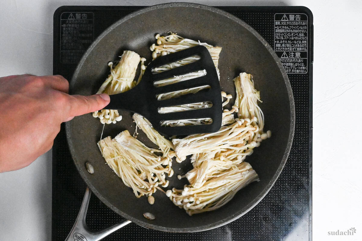 pressing enoki mushrooms flat with a spatula in a frying pan