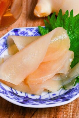 Homemade gari (Japanese pickled sushi ginger) on a white and blue plate decorated with a Perilla leaf on a wooden background