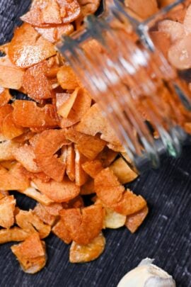 crispy garlic chips falling out of a glass jar onto a black wood-effect surface