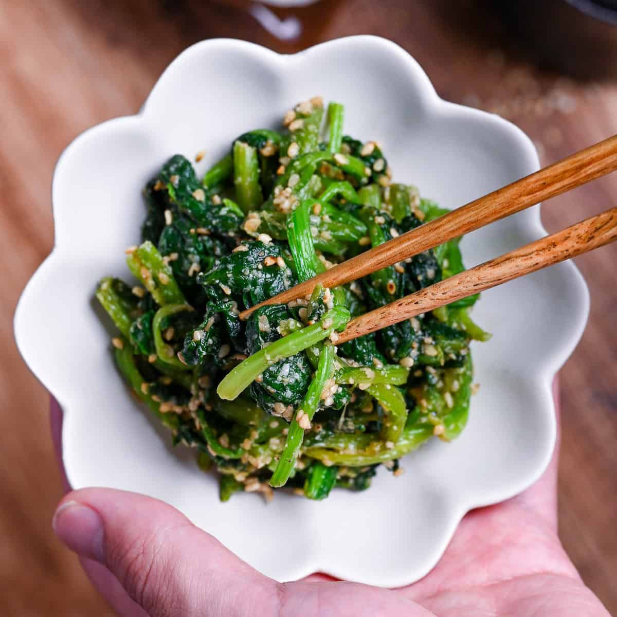 Japanese Sesame Spinach Salad (Horenso Goma Ae) in a white bowl in a hand with wooden chopsticks