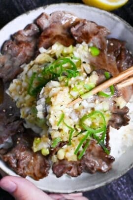 picking up gyutan covered with negi shio sauce with wooden chopsticks