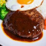 Japanese hamburg steak (hambagu) coated with homemade sauce on a white plate served with rice, vegetables and a fried egg thumbnail