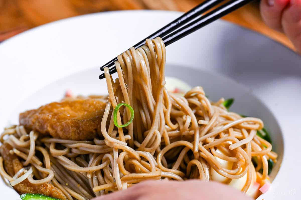 Black chopsticks holding up soba noodles from hiyashi kitsune soba