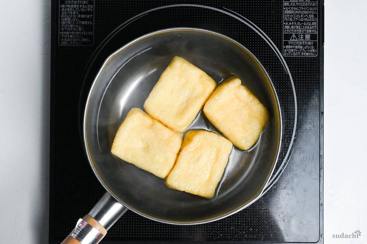 Four pieces of twice fried tofu pouches (aburaage) in a pot of boiling water on the stove top