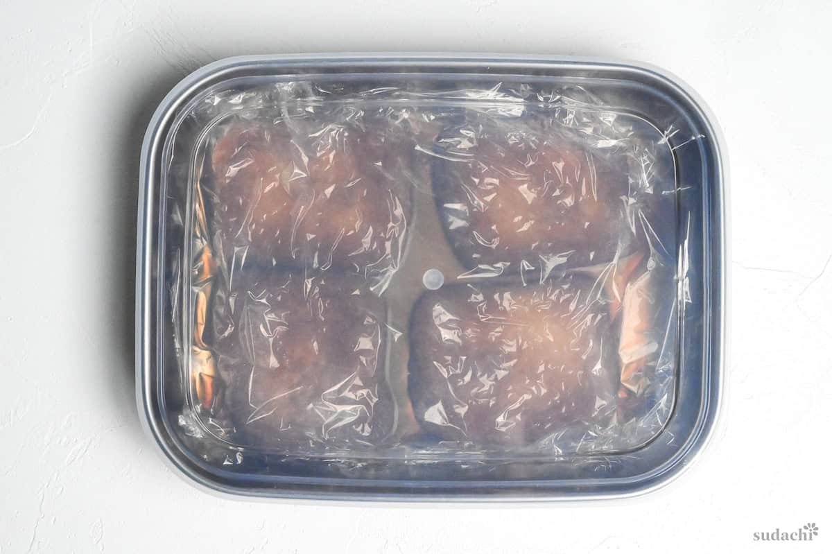 Four pieces of marinated twice fried tofu pouches (aburaage) in a container topped with plastic wrap with lid on top