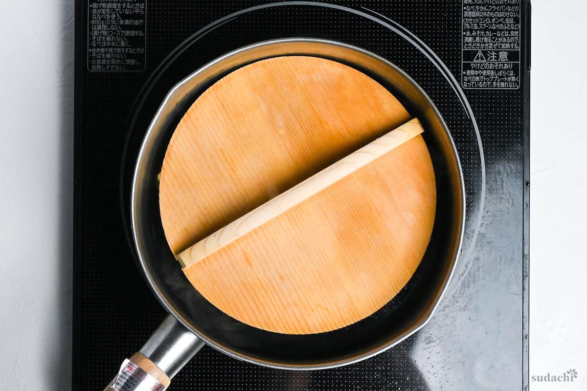 A pot with aburaage (twice fried tofu pouches) submerged with wooden drop lid on top