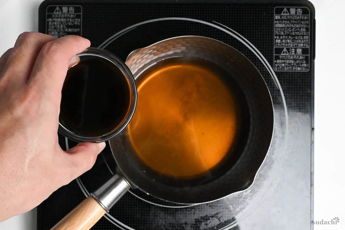 Adding light soy sauce to kitsune tofu marinade in a pot on the stove top
