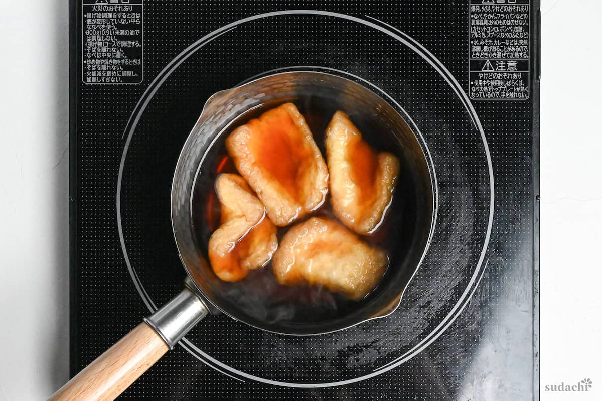 Four pieces of twice fried tofu pouches (aburaage) cooking in kitsune marinade in a pot on the stove top