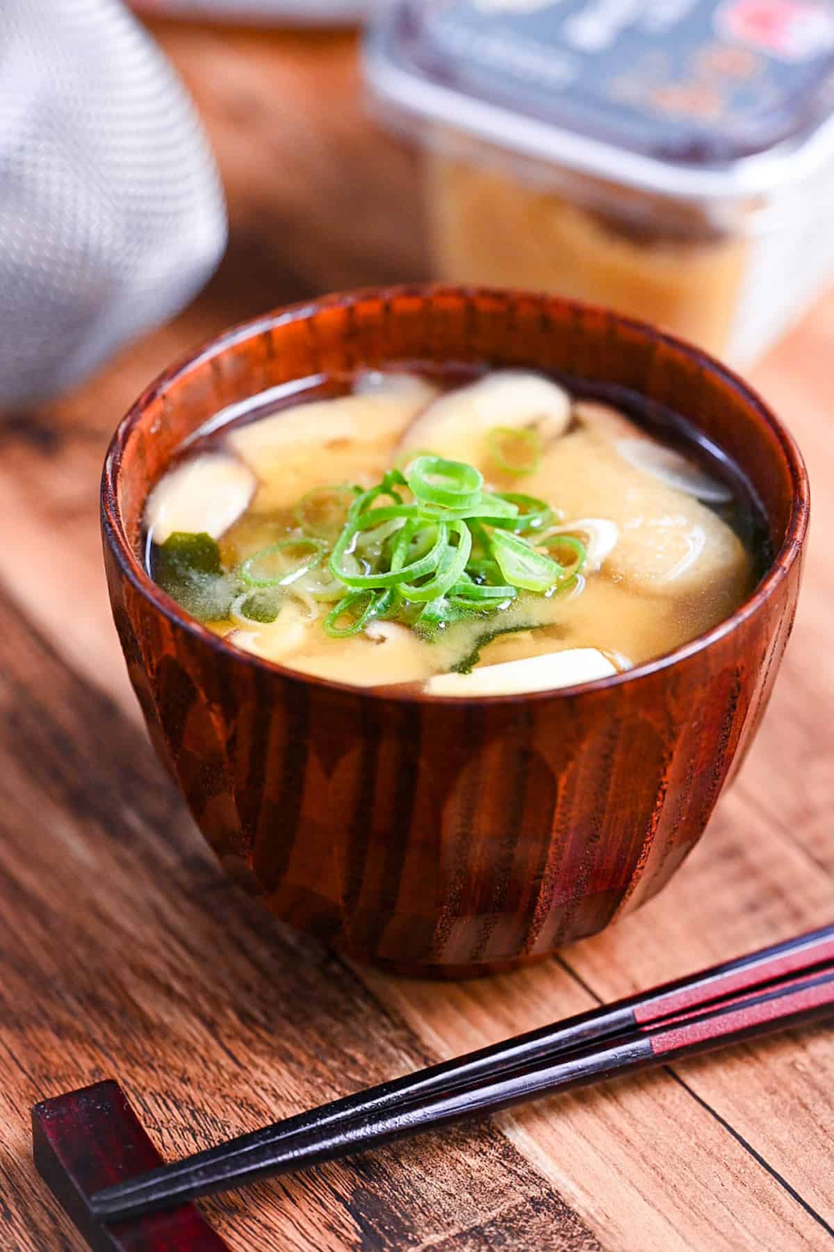 homemade Japanese miso soup in a dark wooden soup bowl with red and black chopsticks