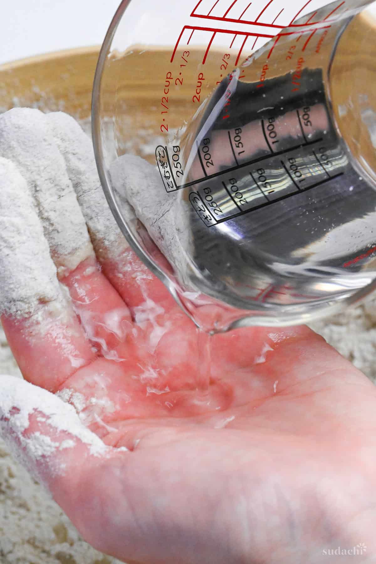 pouring water into hand before incorporating it into soba flour and wheat flour mixture