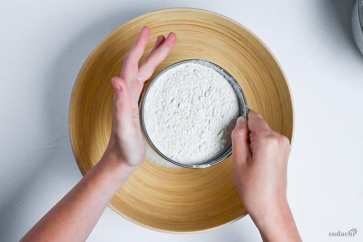 sifting a mixture of buckwheat flour and wheat flour into a large wooden bowl