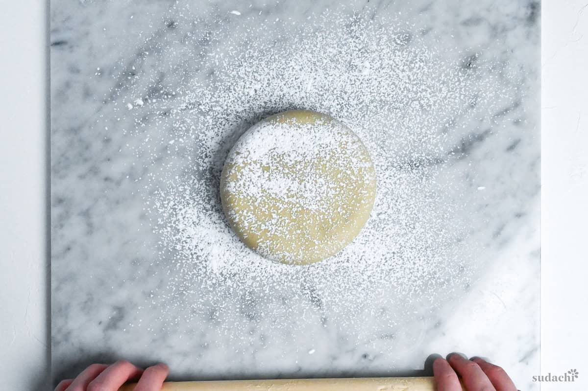 soba noodle dough pressed into a disc shape and dusted with flour on a marble kneading board