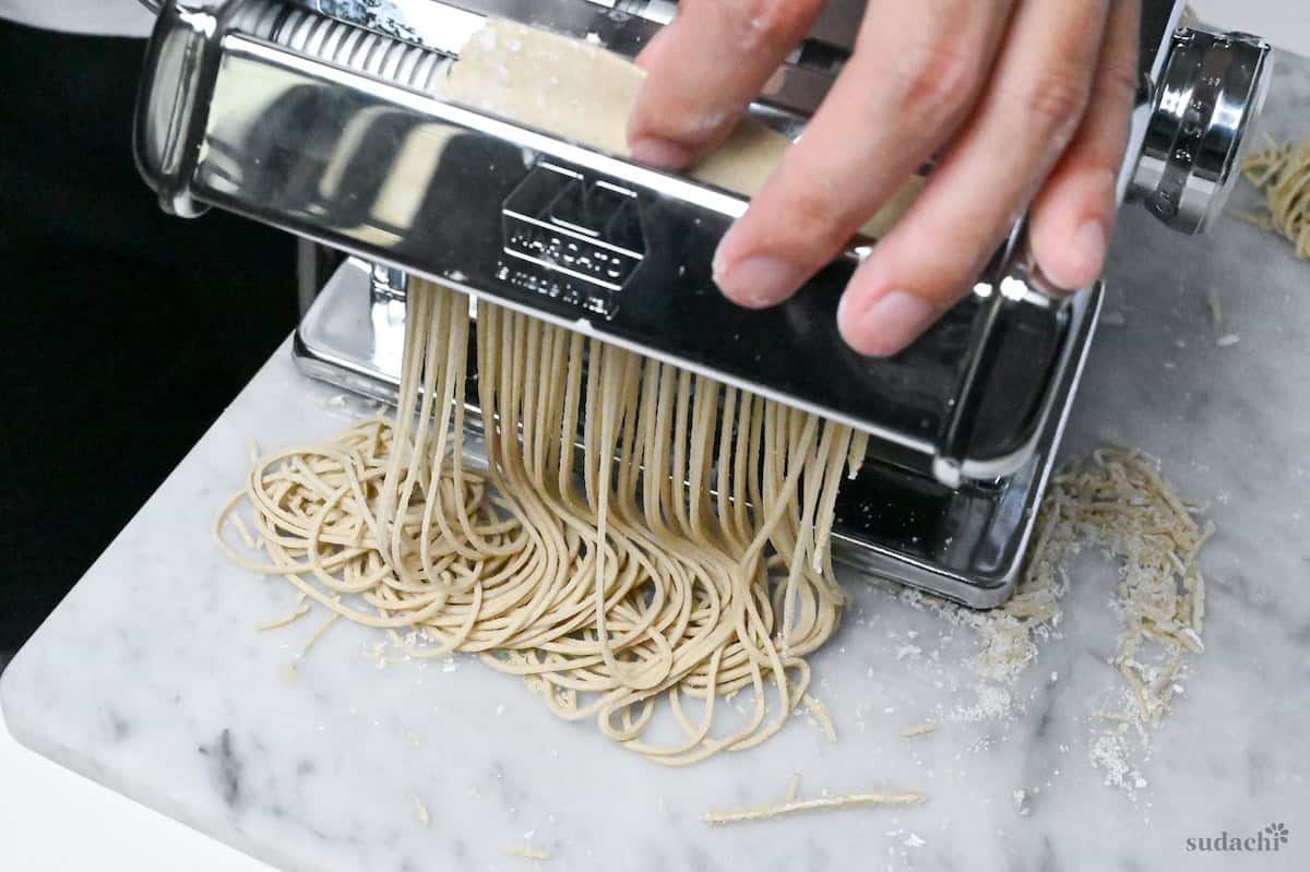feeding soba noodle dough through a cutting attachment on a pasta machine