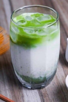 iced matcha latte with matcha whisk and small white bowl of matcha powder