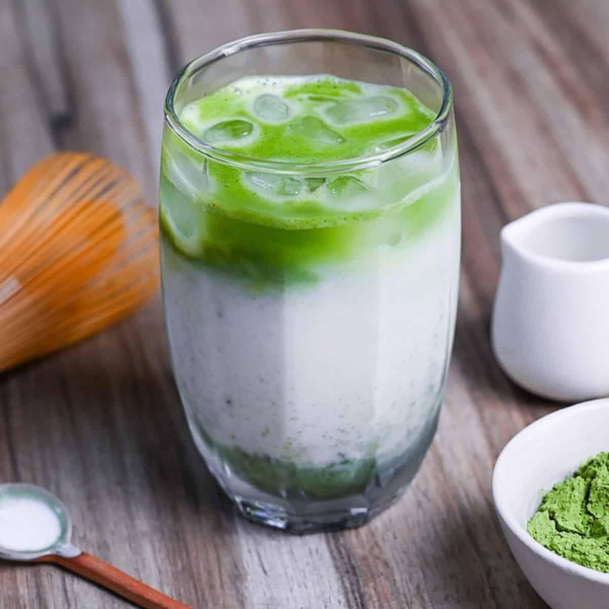 iced matcha latte with matcha whisk and small white bowl of matcha powder