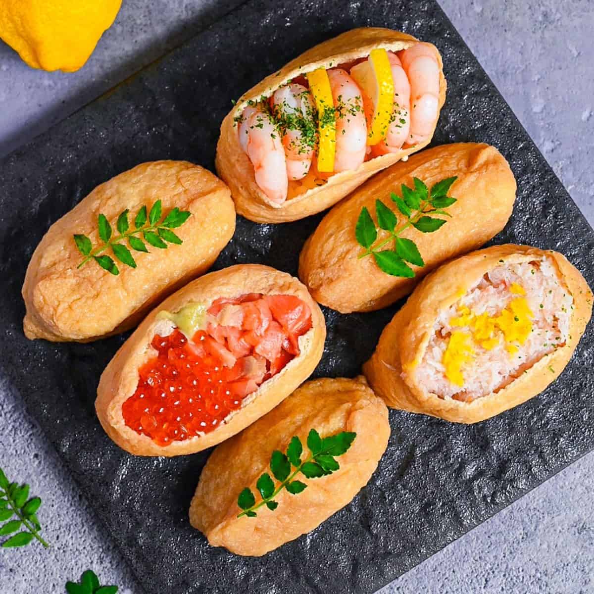 Inarizushi (inari sushi/ stuffed tofu touches) with various toppings on a slate style square plate