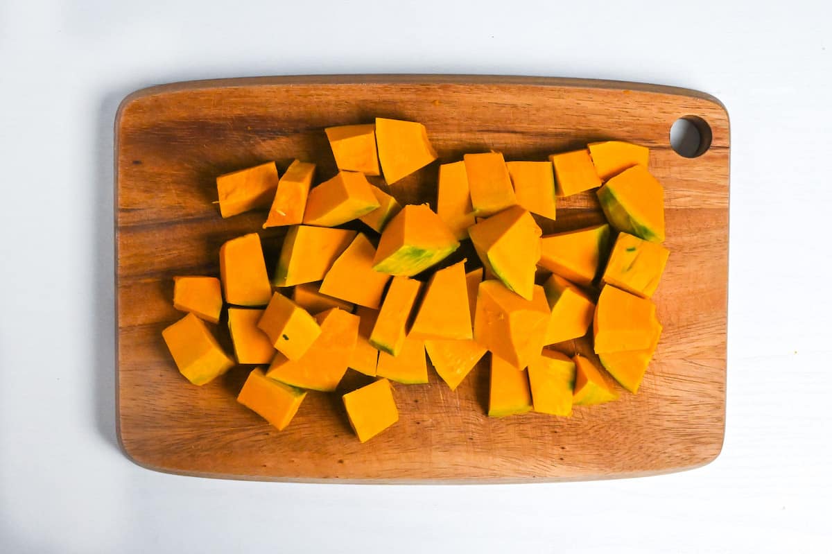 peeled kabocha cut into cubes on a wooden chopping board