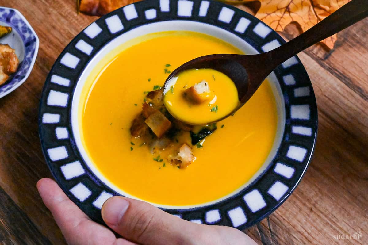 Japanese style kabocha soup in a white bowl with blue patterned rim, scooped with a wooden spoon