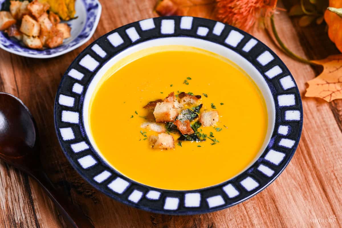 Japanese style kabocha soup topped with homemade croutons and kabocha skin in a white bowl with blue patterned rim