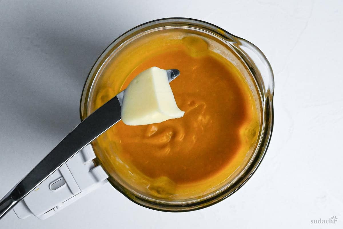 adding butter to smooth kabocha soup in a blender