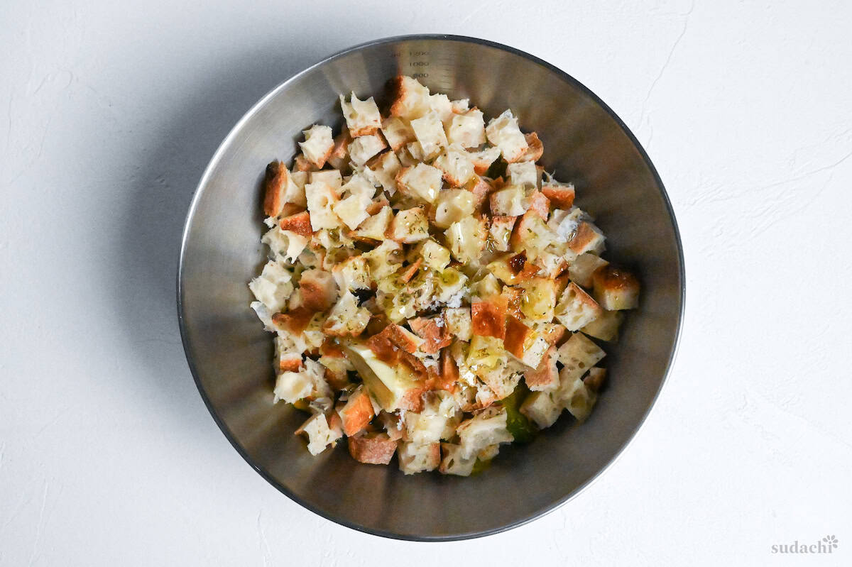 cubed baguette with olive oil and mixed herbs in a steel bowl