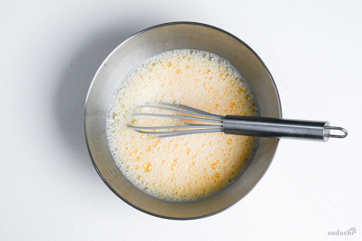 whisked egg and chilled water in a mixing bowl with silver whisk