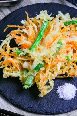 Kakiage (Japanese mixed vegetable tempura) on a slate plate next to a small heap of coarse salt for dipping