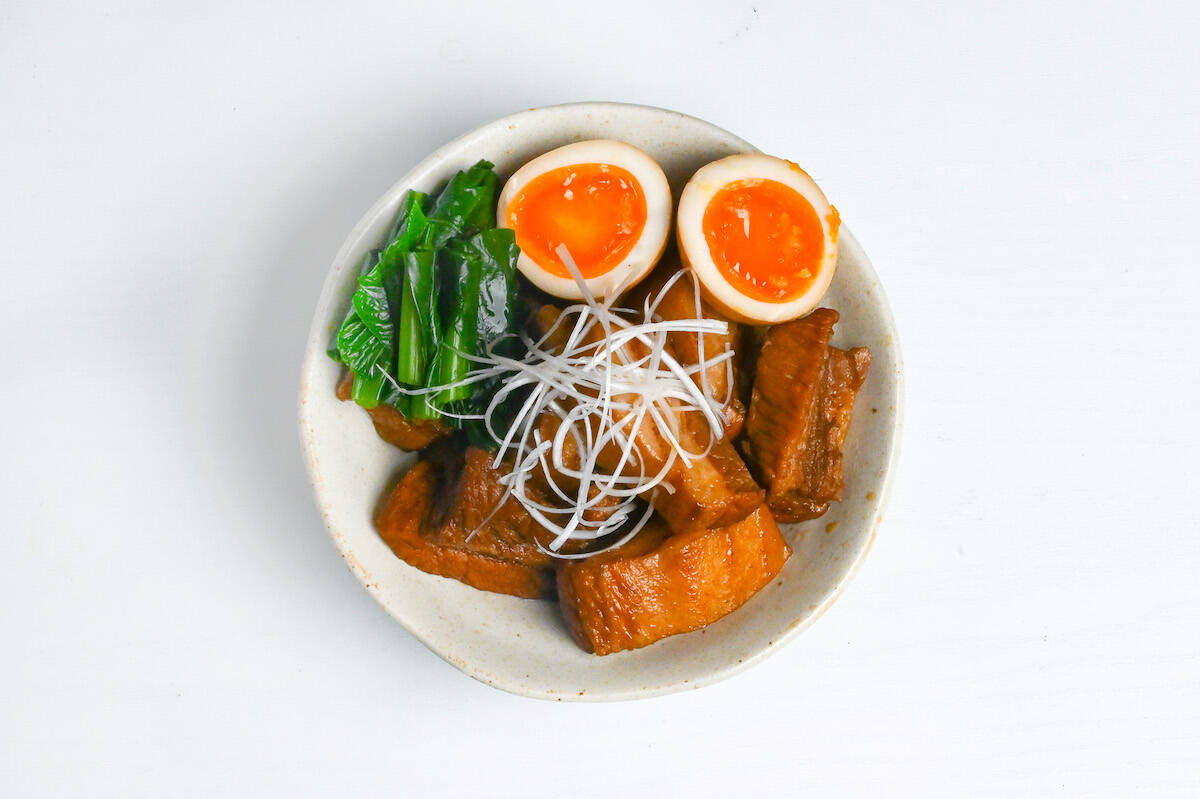 buta no kakuni in an off-white dish next to soft boiled eggs and greens topped with shiraganegi