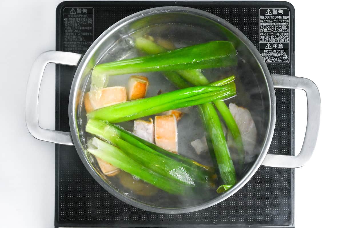 chunks of pork simmering in stock with green onion