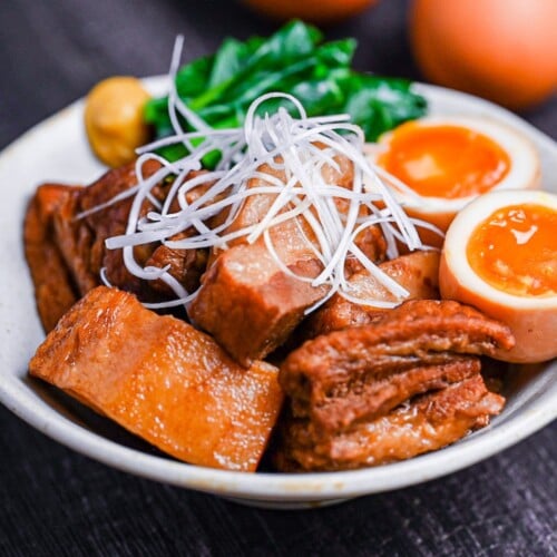 Buta no kakuni (Japanese braised pork belly) in an off-white dish with marinated soft boiled eggs, mustard spinach and a blob of mustard topped with shredded green onion