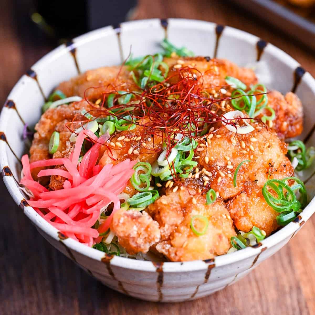 karaage don (Japanese fried chicken bowl) topped with sweet sauce, sesame seeds, chopped green onion, chili threads and pink pickled ginger.