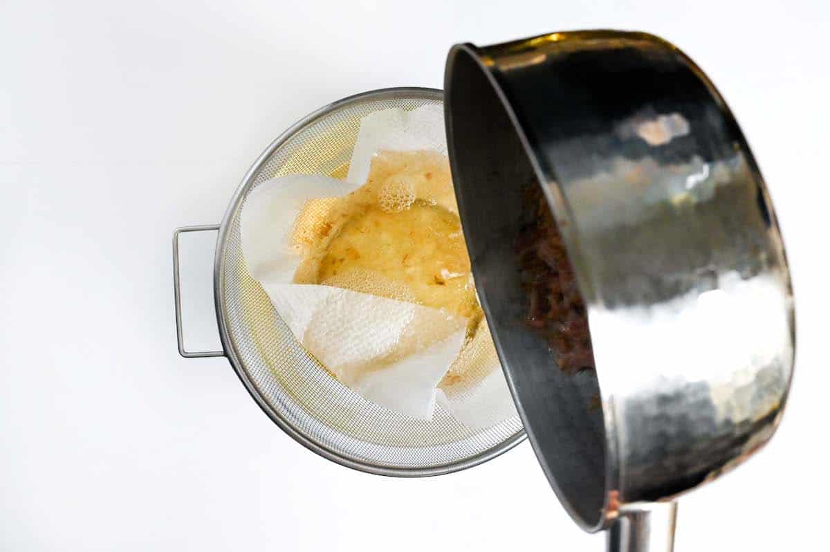 Straining second batch of katsuodashi using a strainer lined with kitchen paper