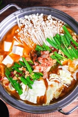 Japanese kimchi nabe with pork, tofu, mushrooms and cabbage topped with garlic chives, fried garlic and chili in an aluminum pot