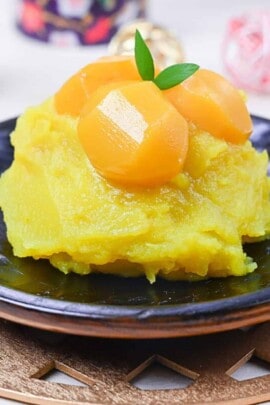 Kuri kinton on a black plate topped with candied chestnuts and a leaf