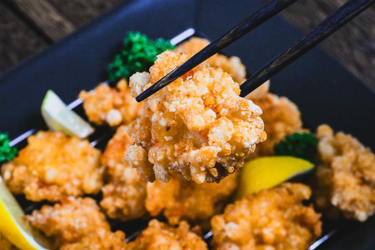 Lemon Karaage (Japanese style fried chicken made with chicken breast coated in a lemon flavored batter) on a black plate decorated with lemon wedges and curly parsley