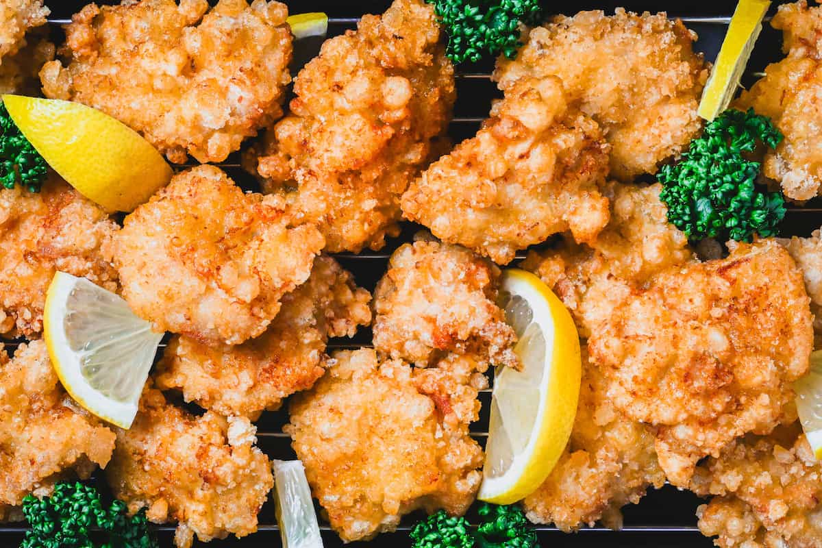Lemon Karaage (Japanese style fried chicken made with chicken breast coated in a lemon flavored batter) on a black plate decorated with lemon wedges and curly parsley