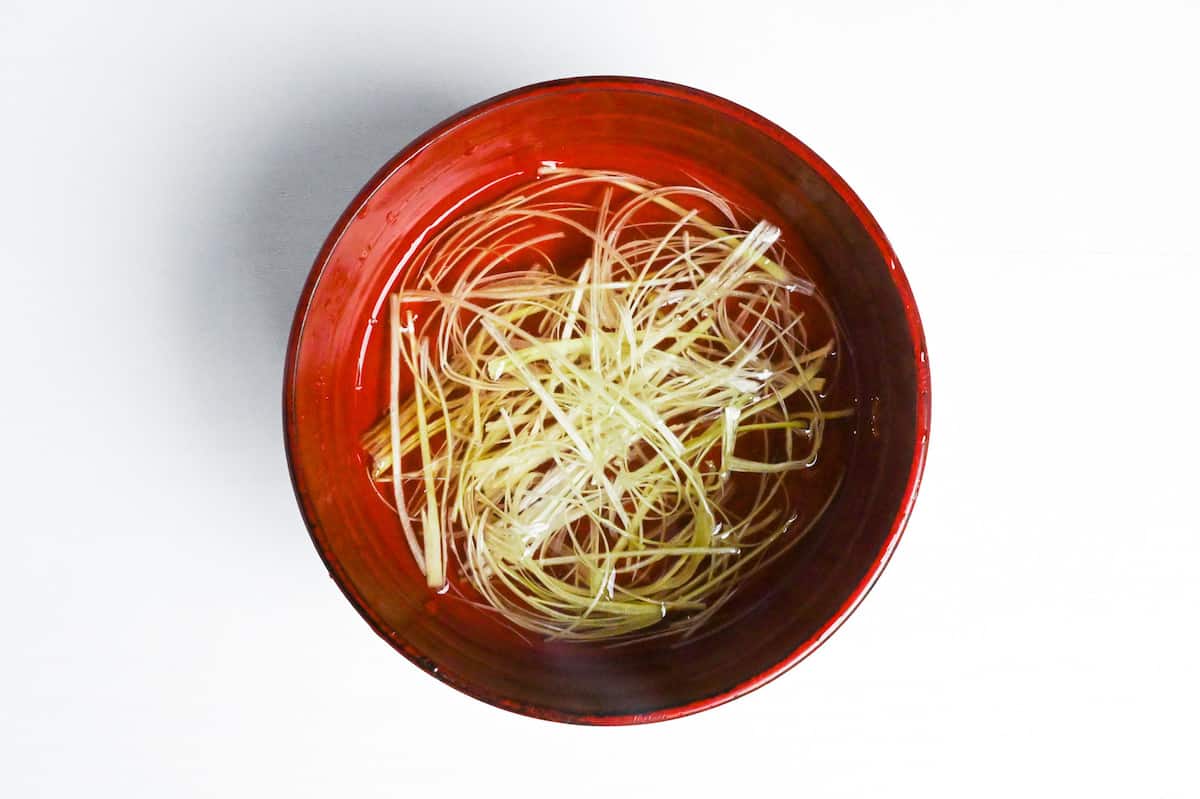 shredded green onion soaking in a red bowl of water