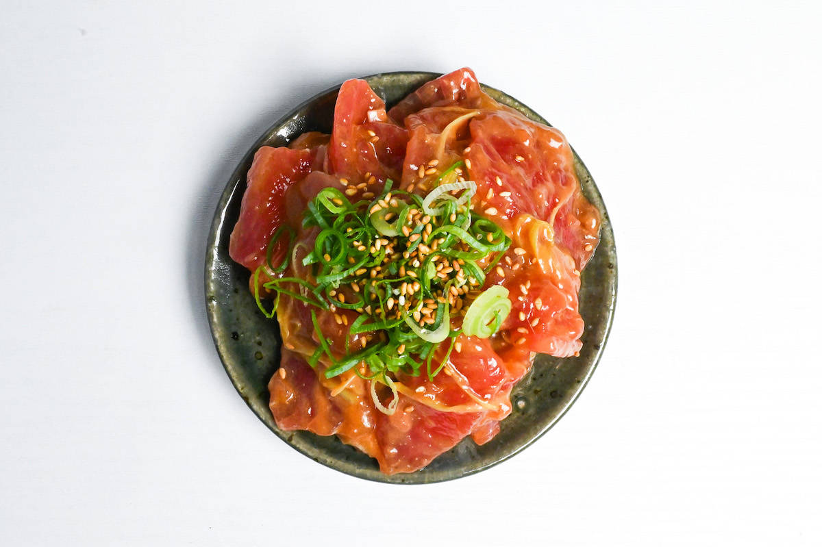 miso marinated tuna sashimi on a green plate topped with chopped green onion