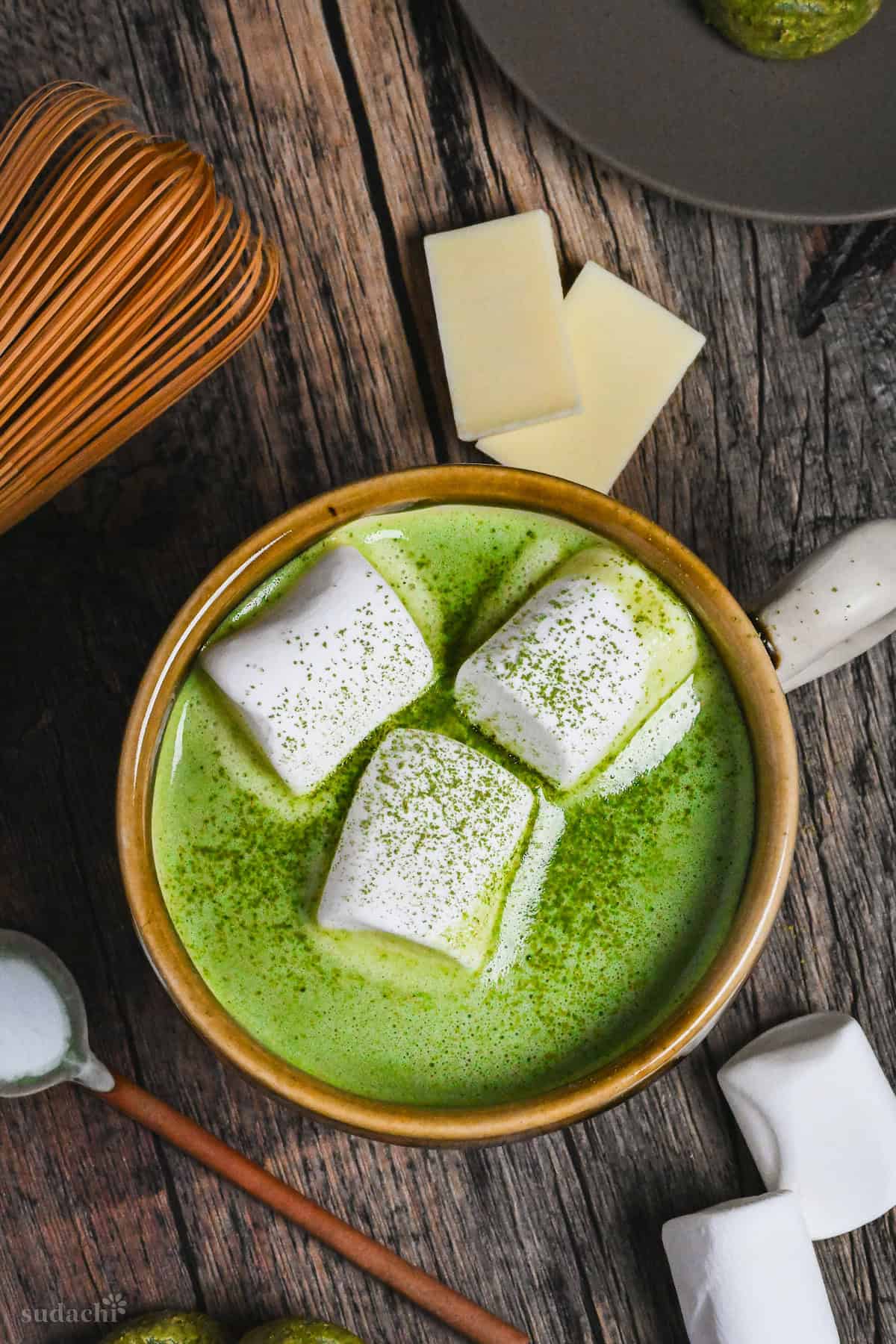 Matcha white hot chocolate in a brown and cream Japanese ceramic mug topped with marshmallows and matcha powder on a dark wooden background
