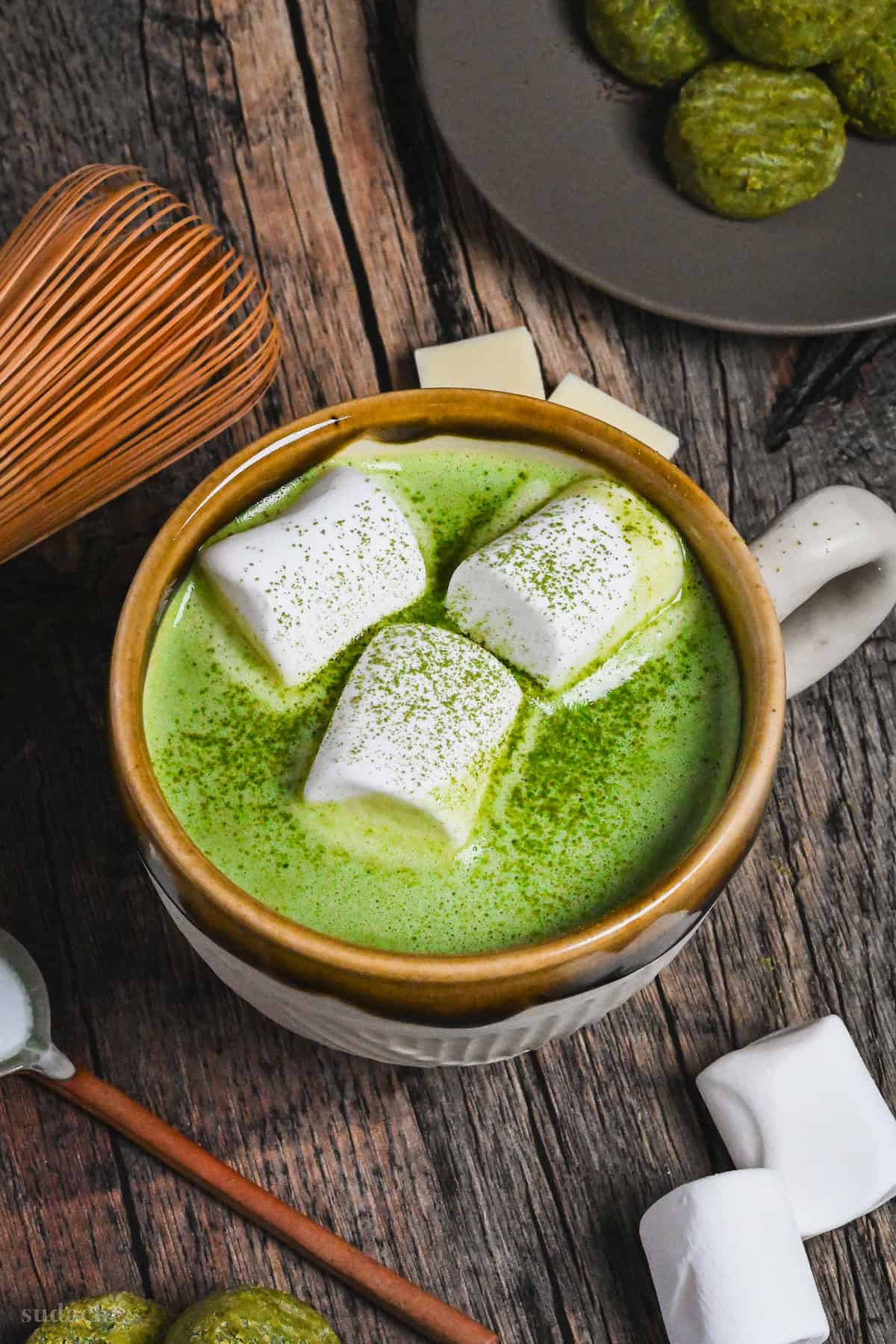 Matcha white hot chocolate in a brown and cream Japanese ceramic mug topped with marshmallows and matcha powder on a dark wooden background