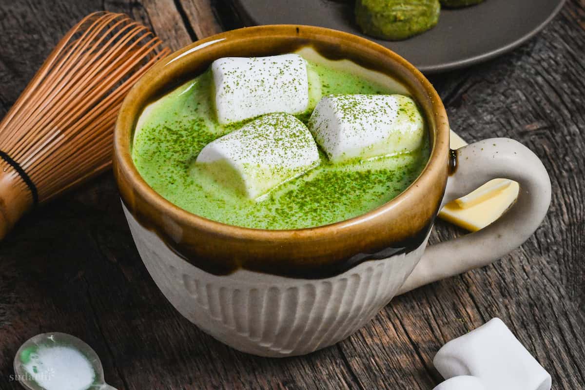 Matcha white hot chocolate in a brown and cream Japanese ceramic mug topped with marshmallows and matcha powder on a dark wooden background