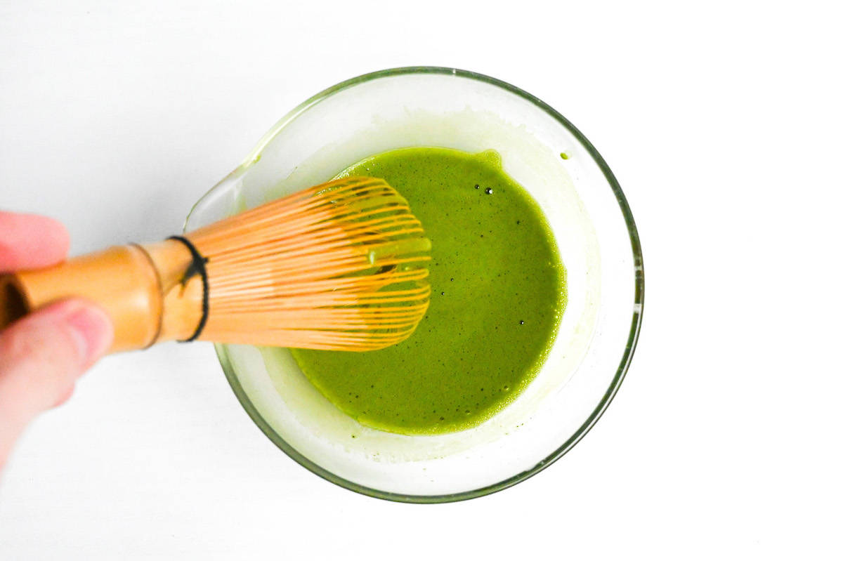 whisking matcha with water in a small glass bowl