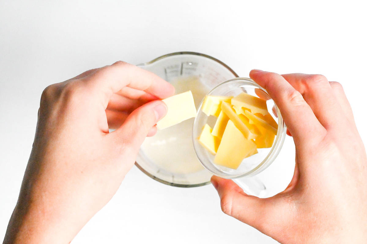 dropping pieces of broken white chocolate into jug of heated milk