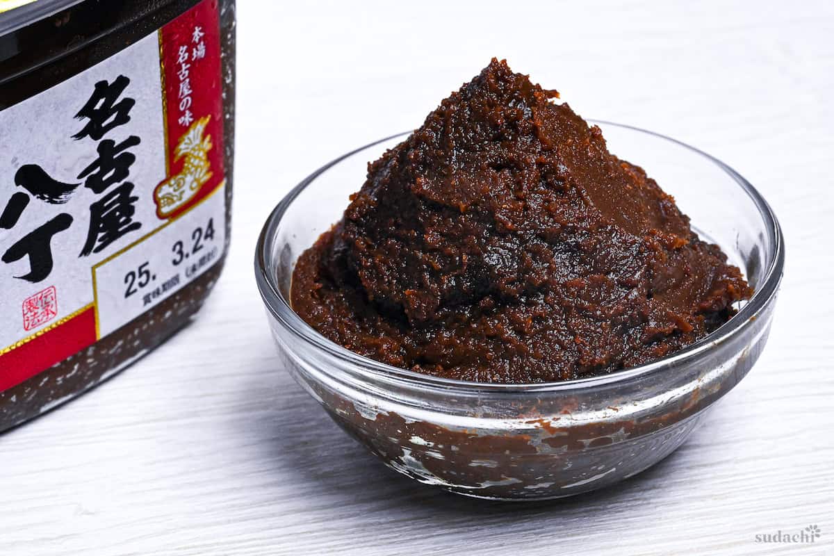 Nagoya style red hatcho miso in a small glass bowl with the branded box in the background