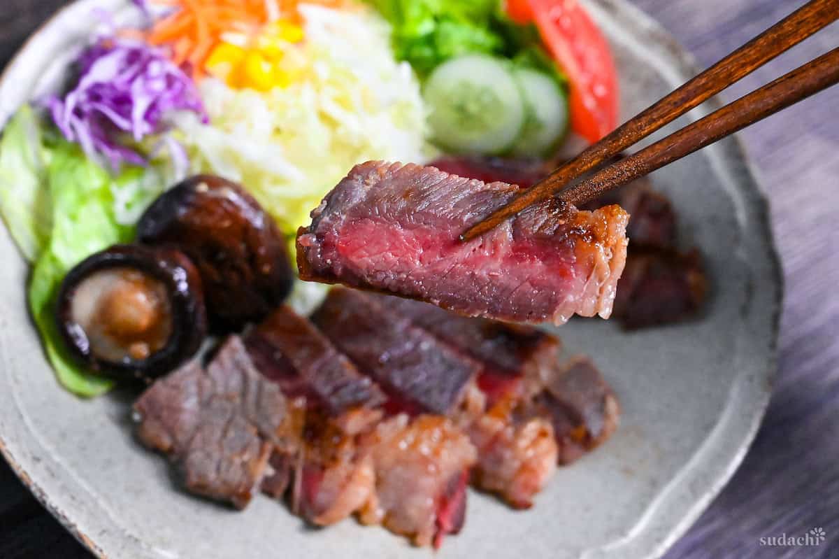 holding a piece of miso marinated steak with wooden chopsticks