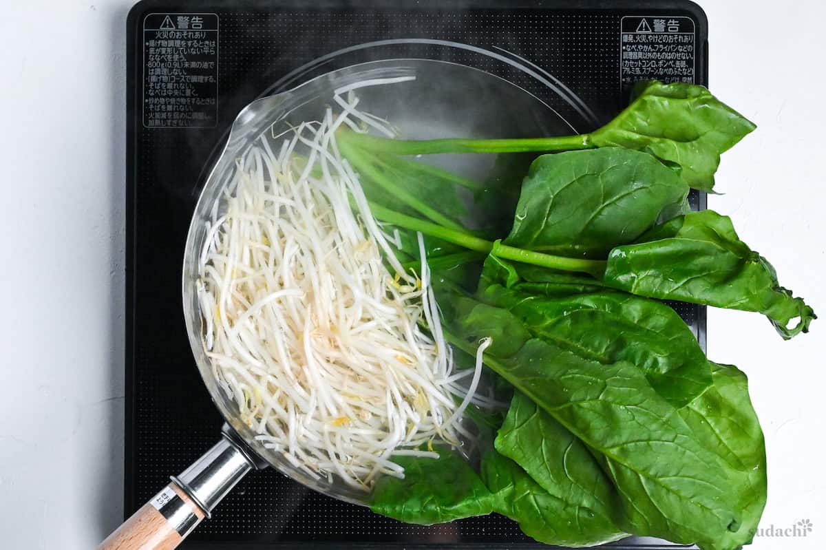 boiling beansprouts and spinach in a pot of water on the stove