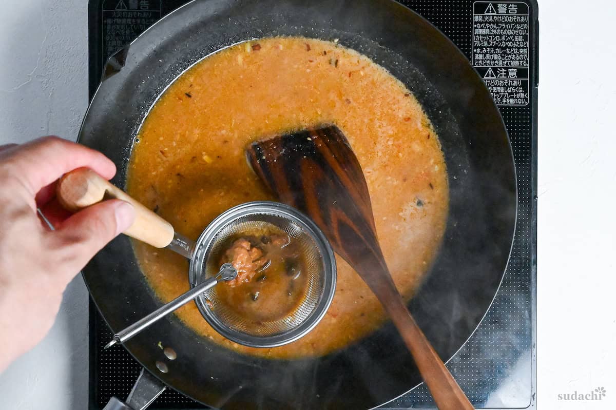 adding miso in miso strainer to soup base in wok