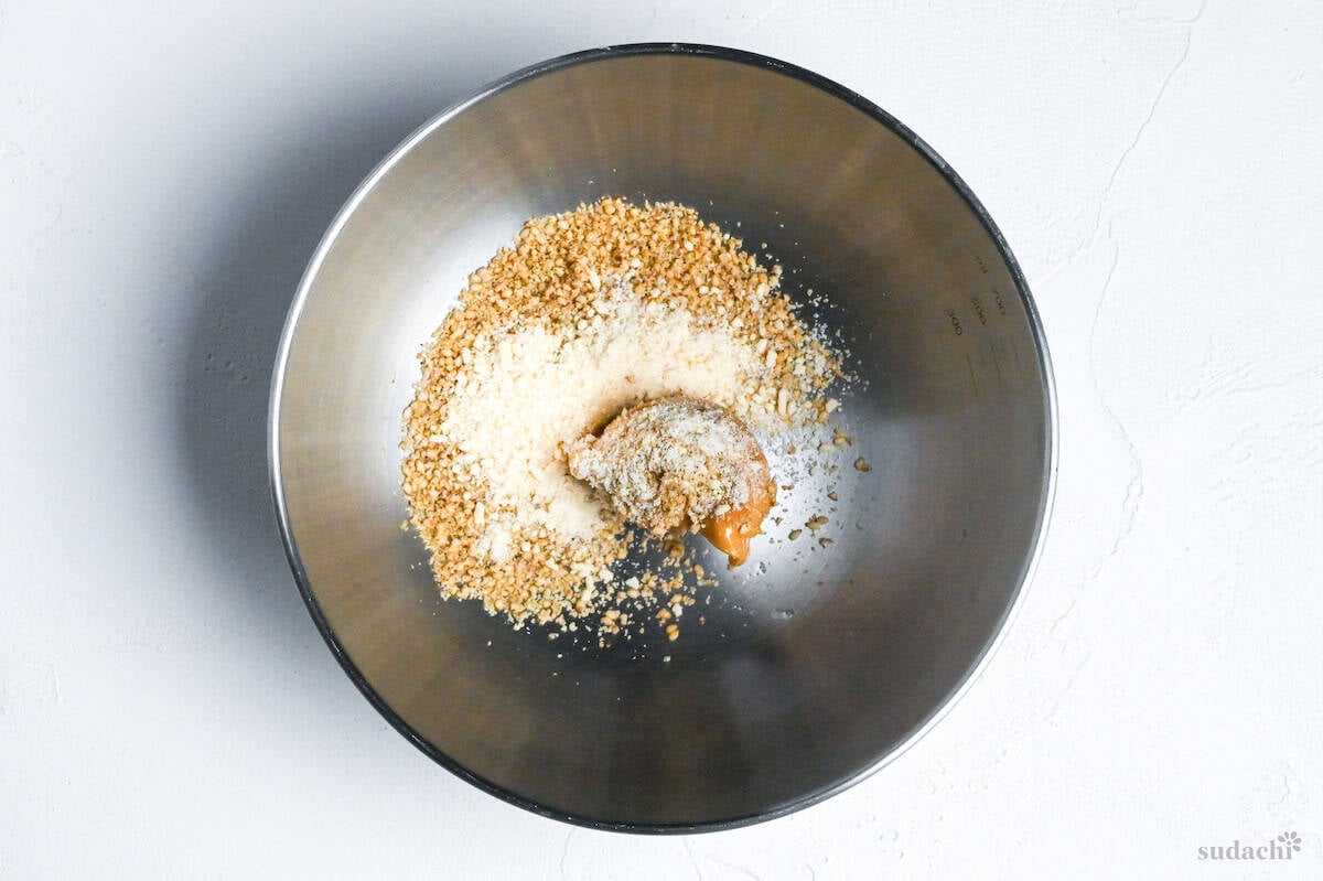 ground sesame seeds, peanut butter and chicken bouillon powder in a steel mixing bowl on a white background