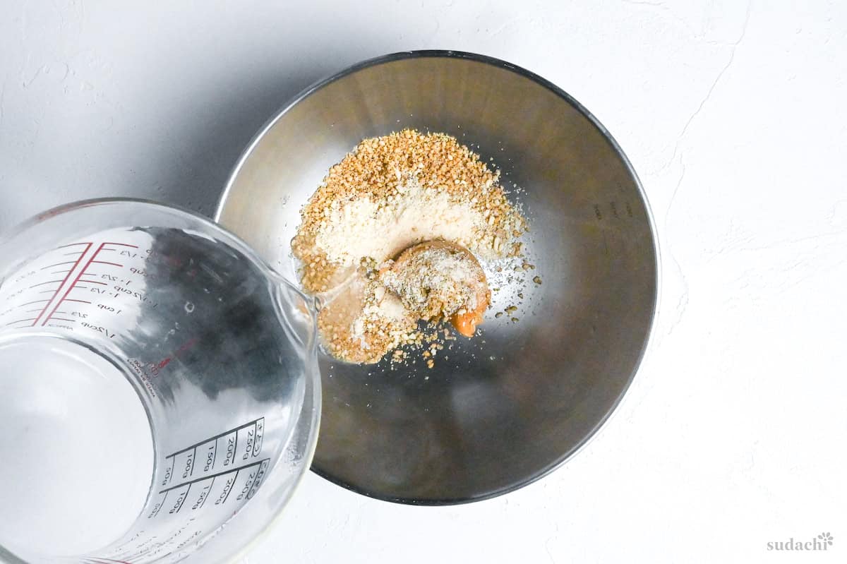 pouring hot water into a bowl with ground sesame seeds, peanut butter and chicken bouillon powder