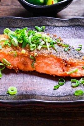 Miso glazed salmon (pan fried) served on a brown rectangular plate and sprinkled with spring onions